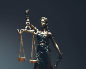 Na zdjęciu widoczna jest figura Temidy, znanej również jako Justitia – personifikacja sprawiedliwości w mitologii greckiej i rzymskiej. W jednej ręce trzyma wagę, która odzwierciedla bezstronne rozważanie argumentów, w drugiej miecz – gotowość do egzekwowania wyroku. To uniwersalny znak niezależności wymiaru sprawiedliwości i uczciwego osądu.